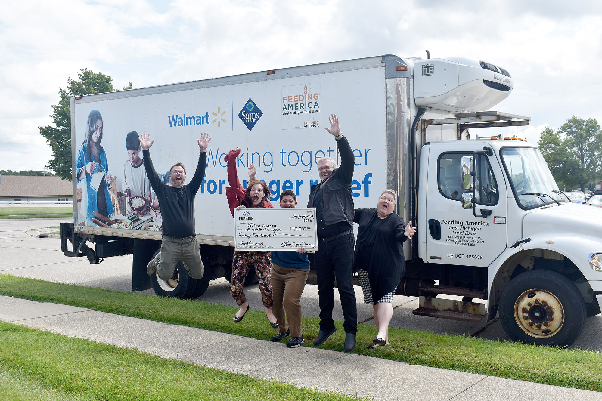 A group of BCF staff jumping infront of a Feeding America box truck with a large check. 