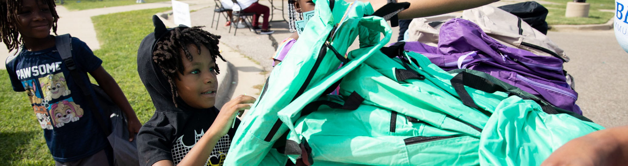 A young boy reaching for a teal backpack.