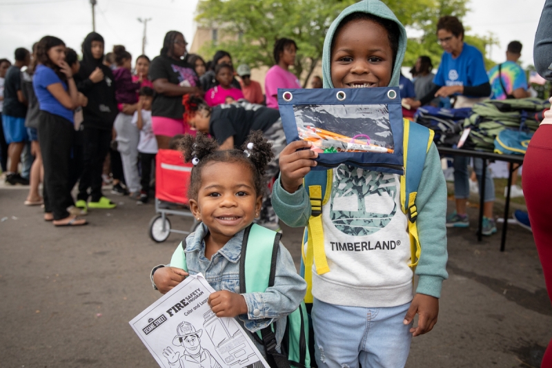 Two young children standing side-by-side holding pencil pouches. 