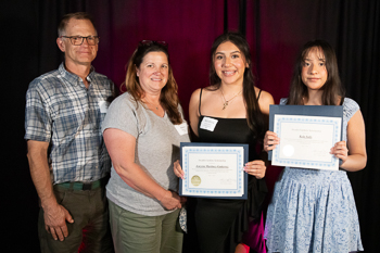 A teenager holding a certificate while standing between two adults. 