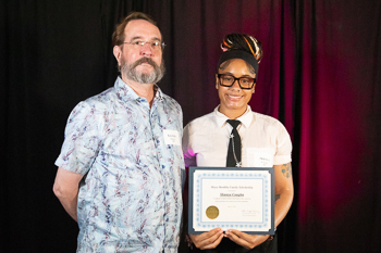 A teenager holding a certificate while standing next to an adult. 