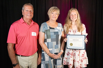 A teenager holding a certificate while standing between two adults. 