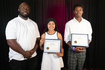 Two teenagers each holding a certificate while standing next to an adult. 