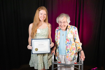 A teenager holding a certificate while standing next to an adult. 