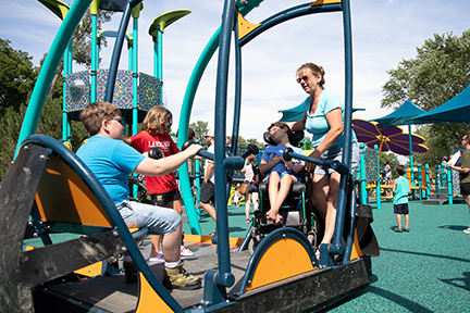 Children swinging on a swing that is accessible for wheelchair users.