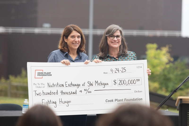 two women stand holding a $200,000 check.