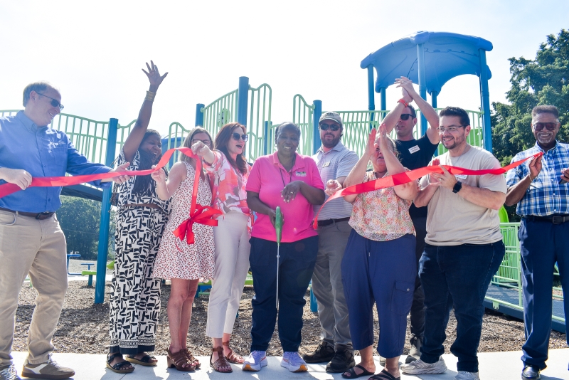A group of people cutting a ribbon in front of the playground.