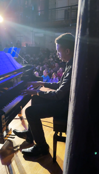 man playing piano with children listening in the background.