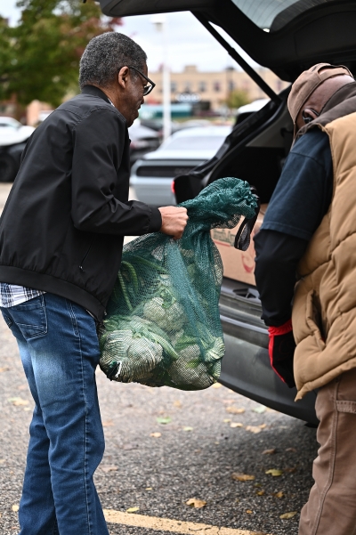 Man loading a bag full of broccoli and cauliflower into the back of a vehicle.