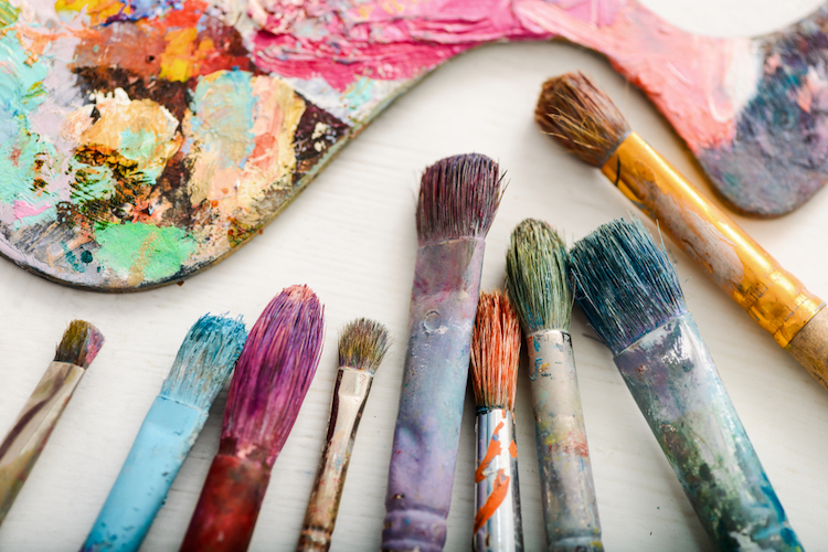 Paintbrushes full of paint laid on a table.