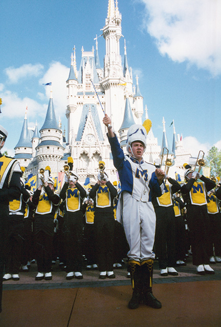 Drum major with arm stretched out in front of him with Disney castle in background.