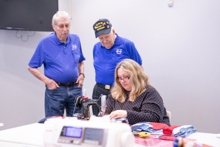 Woman sewing with two veterans watching. 