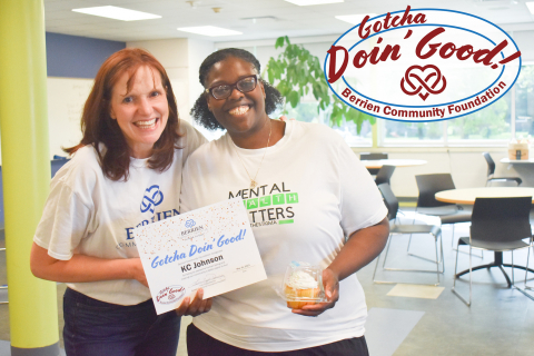 Two women standing side-by-side, one holding a cupcake and the other holding a certificate acknowledging the acts of kindness KC Johnson does. 